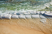 Sandsäcke in Reihen am Wasserrand, um die Erosion des Strandes zu verhindern