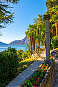 Walkway with Column on Lake Lugano with Mountain Peak and Palm Tree in a Sunny Day with Clear Sky in Lugano, Ticino, Switzerland.