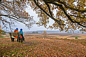 Mann und Frau beim Wandern machen Rast und schauen auf herbstliche Heide, Heidschnuckenweg, Undeloh, Lüneburger Heide, Niedersachsen, Deutschland