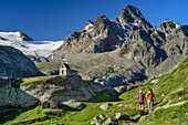 Man and woman hiking towards chapel, Grand Assaly in background, Rifugio Deffeyes, Rutor Group, Graian Alps, Aosta, Italy