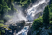 Zwei Personen stehen auf Brücke vor Rutor-Wasserfällen, Rutorfälle, Rutorgruppe, Grajische Alpen, Aosta, Italien