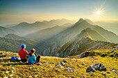 Man and woman hiking sitting on the summit and looking over the Karawanken, Veliki vrh, Hochturm, Karawanken, Slovenia, Carinthia, Austria