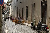 Eine Straße mit Menschen, die vor einem Restaurant sitzen und das Mittagessen in Lissabon, Portugal genießen