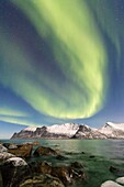 Nordlichter auf schneebedeckten Gipfeln und eisigem Meer entlang des Mefjords, gesehen vom Dorf Mefjordvaer Senja Tromsø Norwegen Europa.