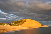 Die Sandsteinfelsen am East Cliff in der Nähe von Bridport an Dorsets Jurassic Coast World Heritage Site, aufgenommen an einem Abend Mitte September vom Pier in West Bay. Eine Langzeitbelichtung wurde verwendet, um die Bewegung im Wasser und in den Sturmwolken zu verwischen.
