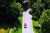 A car makes its way down a country lane in an aerial view.
