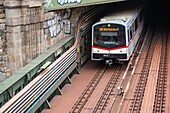 Der U-Bahn-Zug kommt aus einem Tunnel und fährt unter der Brücke Zollamtssteg hindurch, während er den Fluss in Wien, Österreich, überquert.