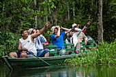 Tourists observe wildlife from a wooden pirogue canoe paddled by Brazilian naturalist guides (front and back), near Manaus, Amazon, Brazil, South America