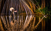 A young woman in a white dress standing in a river at night extends her hand to catch a falling spark, Kapaa, Hawaii, United States of America, Pacific