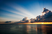 Clouds and sunlight above ocean at sunrise