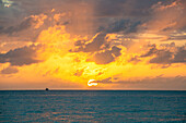 Dramatischer Himmel bei Sonnenuntergang über dem Meer mit Fischerboot in der Ferne