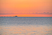 Calm sea at sunrise with fishing boat in distance