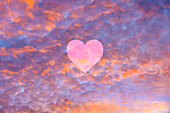 Heart shape against purple and orange clouds