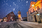 Polen, Karpatenvorland, Rzeszow, beleuchtete Straße mit Kirche im Winter Schneefall in der Nacht