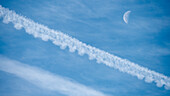 Airplane contrails and waning moon against blue sky