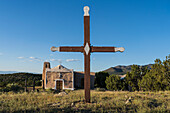 USA, New Mexico, Golden, Wooden cross in front of small San Francisco de Assis church in rural landscape