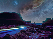 USA, Arizona, Monument Valley Tribal Park, Autos leuchten nachts auf der unbefestigten Straße im Monument Valley