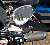 Reflection of snowy trees in wing mirror of motorbike