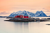Isolierte rote Fischerhütten auf Felsen im kalten Meer bei Sonnenuntergang, Svolvaer, Nordland County, Lofoten-Inseln, Norwegen, Skandinavien, Europa