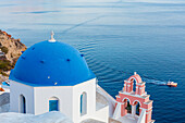 Blue domed white church overlooking boat in Aegean Sea, Santorini, Cyclades, Greek Islands, Greece, Europe