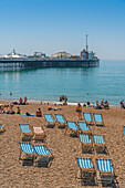 Blick auf Brighton Palace Pier und blau-weiß gestreifte Liegestühle am Strand, Brighton, East Sussex, England, Vereinigtes Königreich, Europa