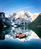 Boote im Pragser Wildsee (Pragser Wildsee) mit Bergen, die sich bei Sonnenaufgang im Wasser spiegeln, Dolomiten, Südtirol, Italien, Europa