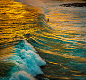 Ein Surfer fängt eine Welle in den goldenen Reflexen des Sonnenuntergangs an der Südküste von Kauai, Hawaii, Vereinigte Staaten von Amerika, Pazifik