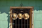 Three straw hats hang on an iron grate in a window, Trinidad, Cuba, West Indies, Central America