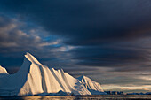 Greenland, Ilulissat, Midnight sun lights massive iceberg grounded near face of Jakobshavn Isfjord on stormy evening