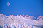 Full moon rising above Glacier National Park Peaks from summit of Big Mountain in winter in Whitefish, Montana, USA.