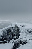 Mann steht am Rand einer schneebedeckten Klippe, Winnats Pass, Castleton, Derbyshire, England