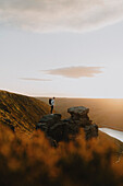 Male hiker on top of rock formation in sunny mountains at sunset, The Trinnacle, Derbyshire, England