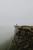 Male hiker at the edge of rocky hilltop in rainy, foggy landscape, Bamford Edge, Derbyshire, England