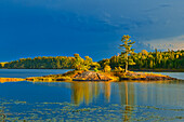 Canada, Ontario, Kenora District. Forest autumn colors reflect on Middle Lake at sunset