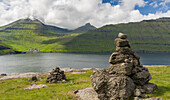 Old traditional cairns, in the background mount Slaettaratindur, the highest peak in the Faroe and village of Funningur located at the Funningsfjordur. Northern Europe, Denmark