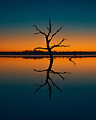 Calm day at a Kansas lake creating reflections of the illuminating blue and orange sky.