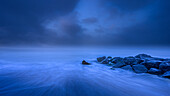 USA, New Jersey, Cape May National Seashore. Nebliger Sonnenaufgang auf Wasser und Felsen