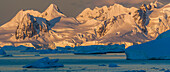 Morning light shines on the mountains of Antarctica, while the icebergs in the ocean remain shadowed.