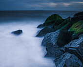USA, New Jersey, Cape May National Seashore. Wellen, die sich bei Sonnenuntergang an Felsen brechen.