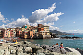 Bathers sunbathe on the rocks in front of the village of Boccadasse, Genoa, Liguria, Italy.