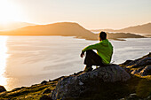 Norwegen, Lofoten, Mann im Sonnenuntergang über dem Fjord