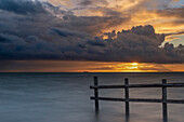 Sonnenuntergnag am Meer. Holzzaun im Wasser. Sonne lukt hinter den Wolken hervor. Lolland, Dänemark, Fehmarn Belt