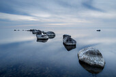 Steine im Wasser liegen im leichten Bogen. Glatte Wasseroberfläche. Wolken speigeln sich im Wasser. Kronvalds Fiskeläge, Klintehman, Gotlands län, Schweden.