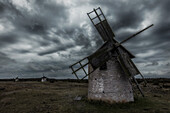 3 alte runde Windmühlen stehen auf steiniger Wiese. Dunkle bedrohliche Wolken, Öland, Schweden.