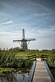 Windmill of Kindedijk in the Netherlands on the water with the blue sky in the background and a wooden bridge in the foreground