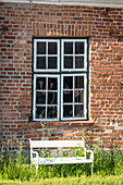 White garden bench in front of a barn window and red brick historic vintage
