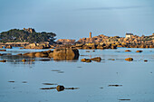 The rocks of the pink granite coast Côte de Granit Rose at the Baie de Sainte Anne near Tregastel looking towards the Maison Gustave Eiffel and the Phare de Ploumanac'h lighthouse , Brittany, France