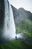 Mann steht am Wasserfall Seljalandsfoss in Island