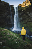 Mann mit gelbem Regenmantel am Wasserfall Kvernufoss in Island