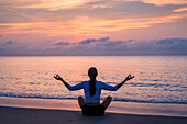 Woman practicing yoga on beach at sunset